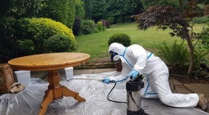 pest controller in hazmat suit spraying furniture outside for woodworm